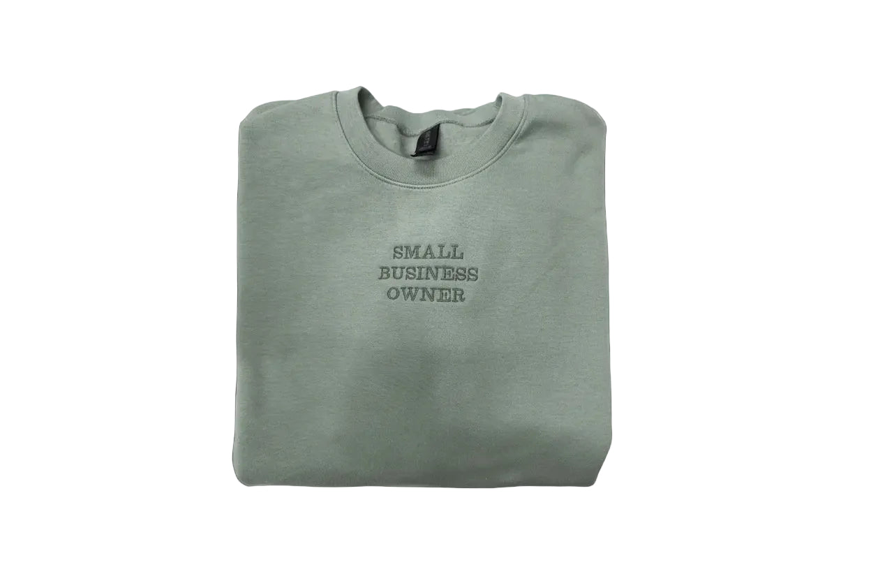 Folded gray sweatshirt with 'Small Business Owner' text on a white surface